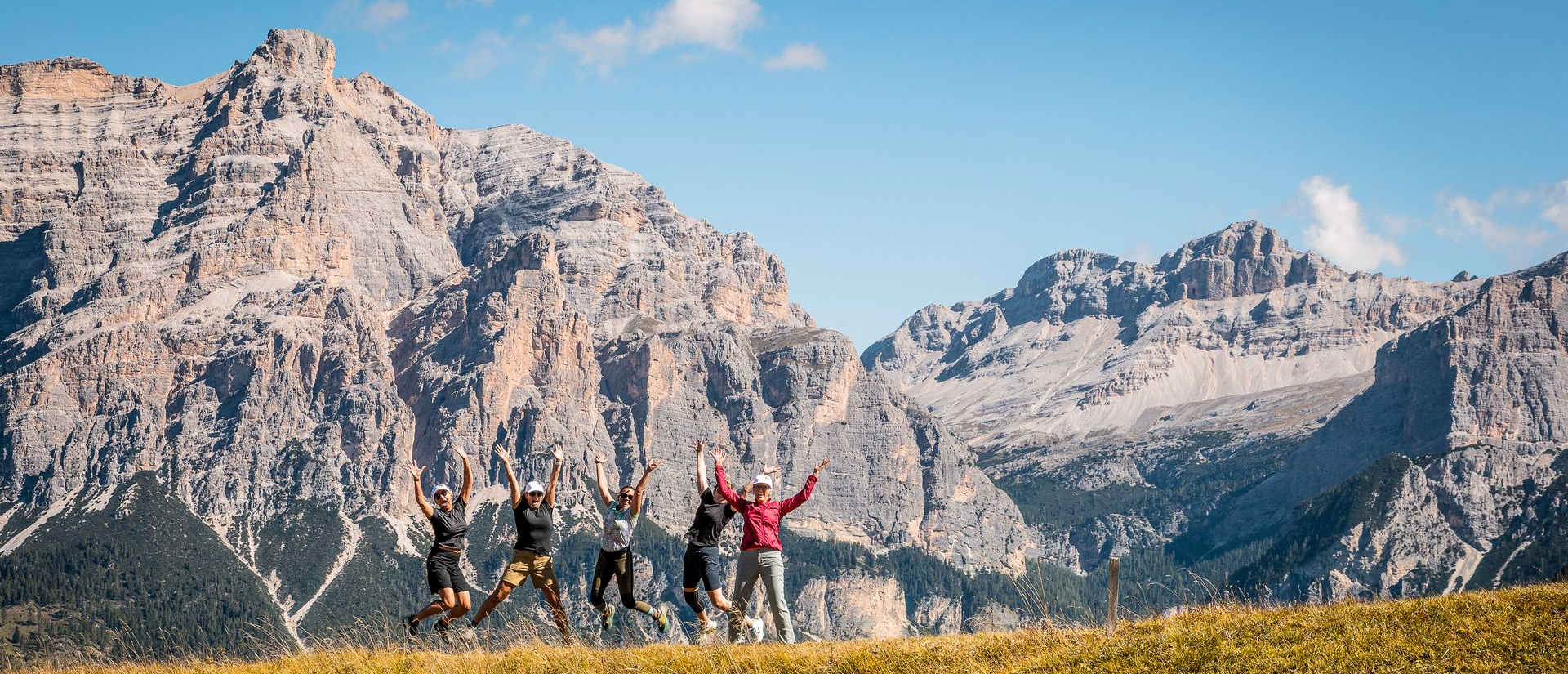 Group of people jumping in front of mountains and a blue sky, happy.