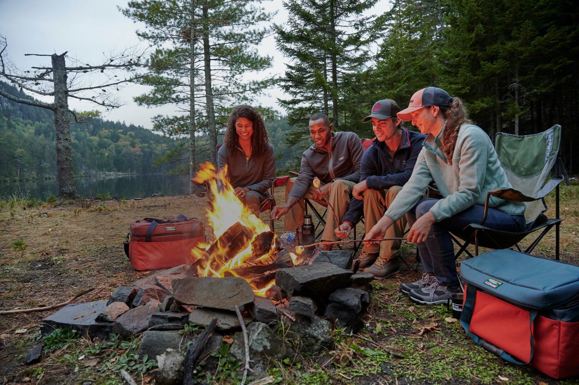 Four friends around a campfire in the forest. They are smiling and roasting something over the flames.