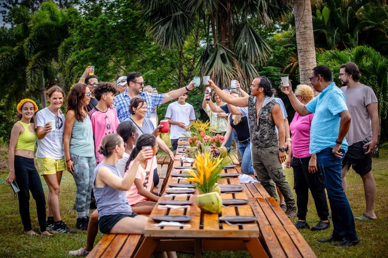 A large group of people are standing around a long wooden picnic table