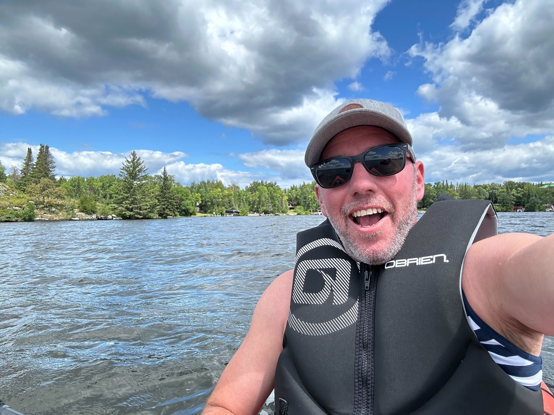 A man wearing a life jacket is taking a selfie on a boat.