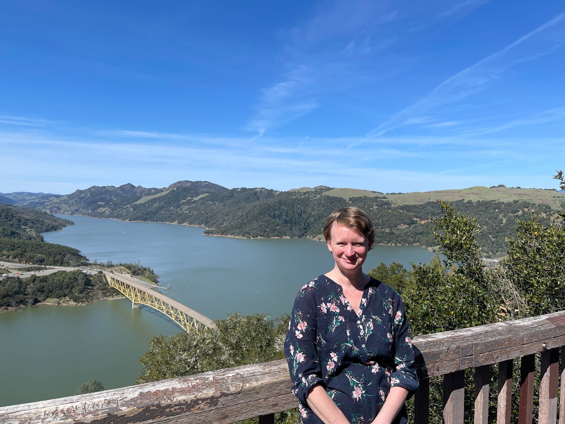 A woman is standing on a balcony overlooking a lake.
