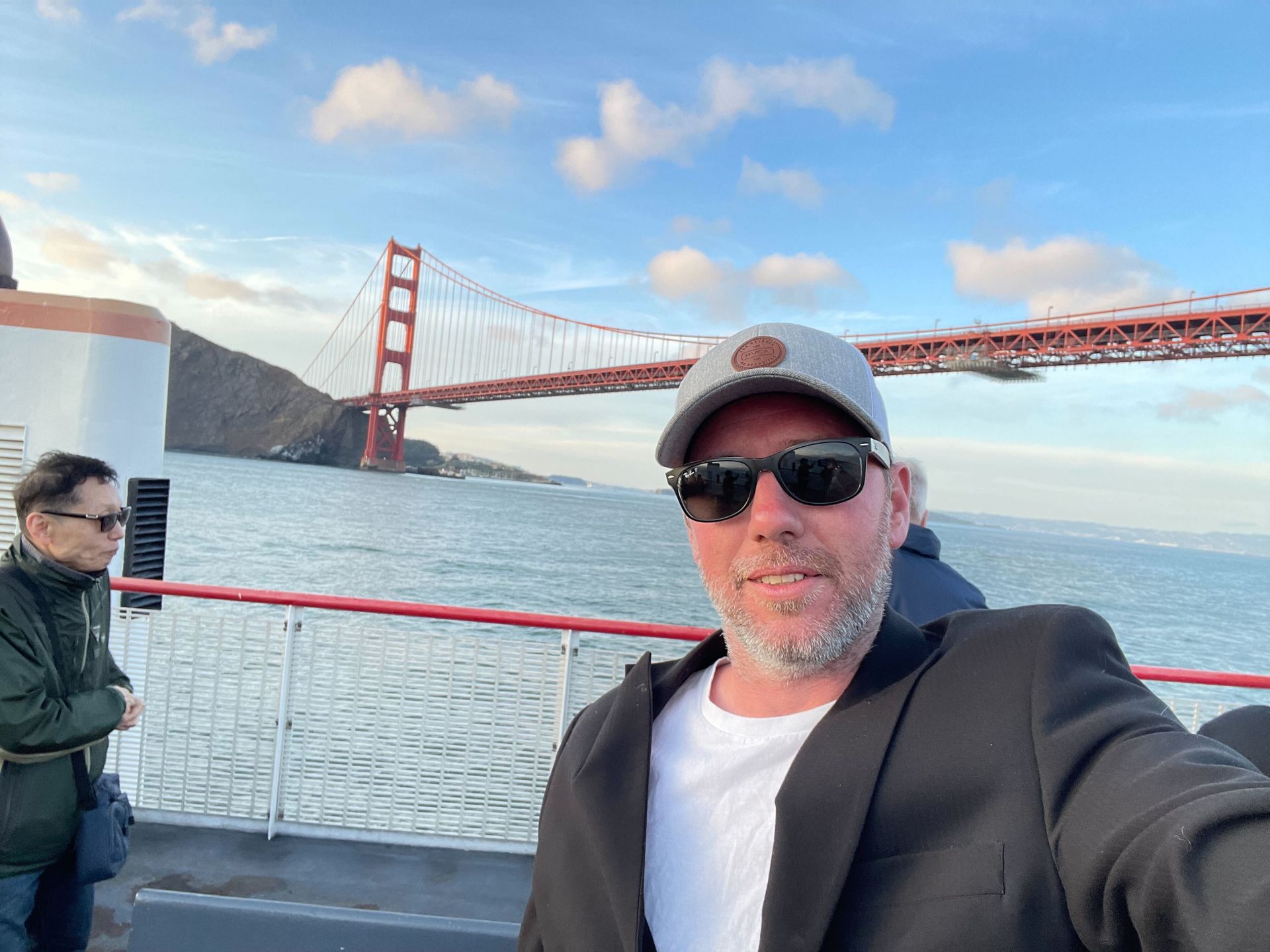 A man is taking a selfie on a boat in front of the golden gate bridge.