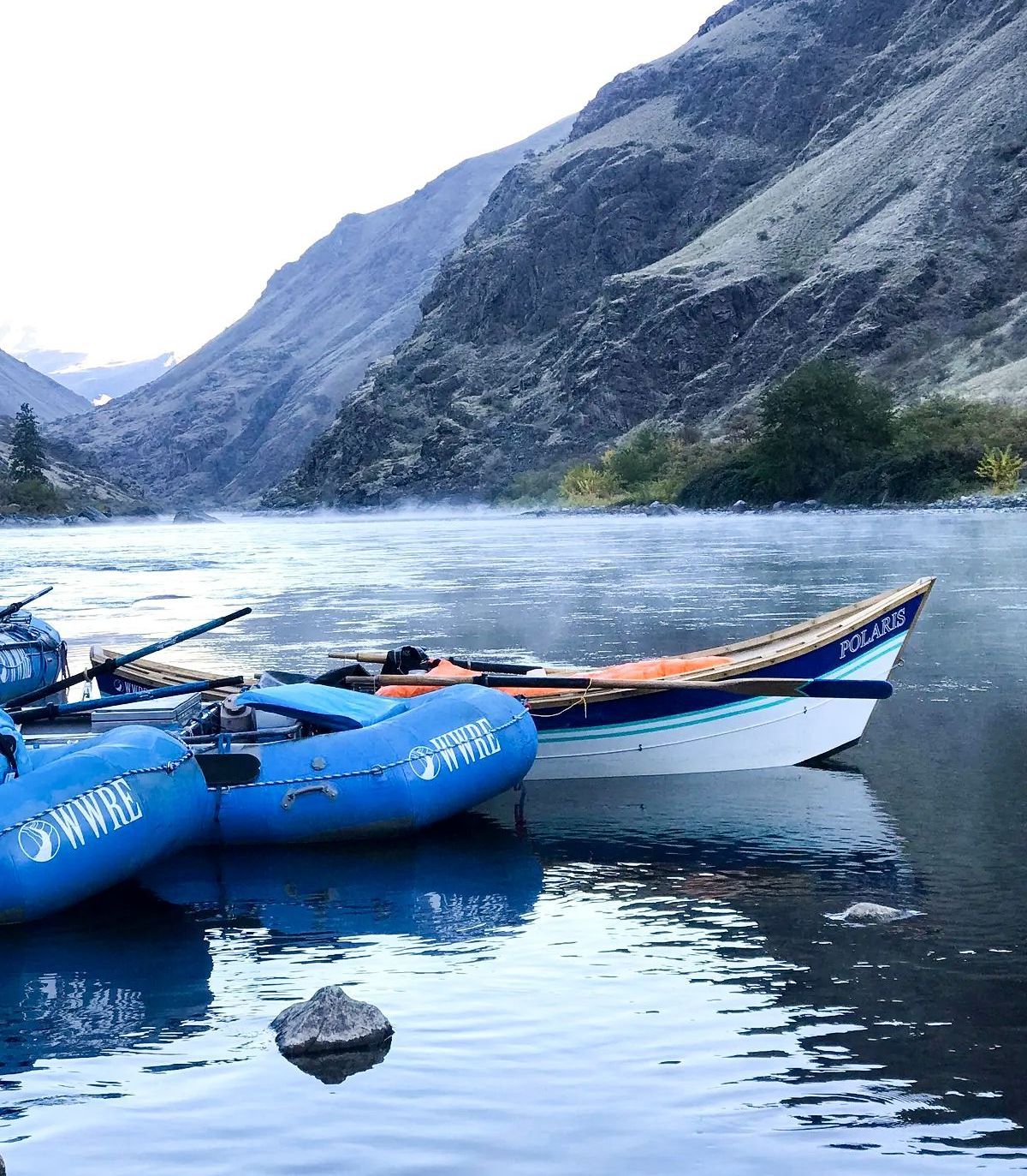 A couple of boats are docked in a river with mountains in the background.