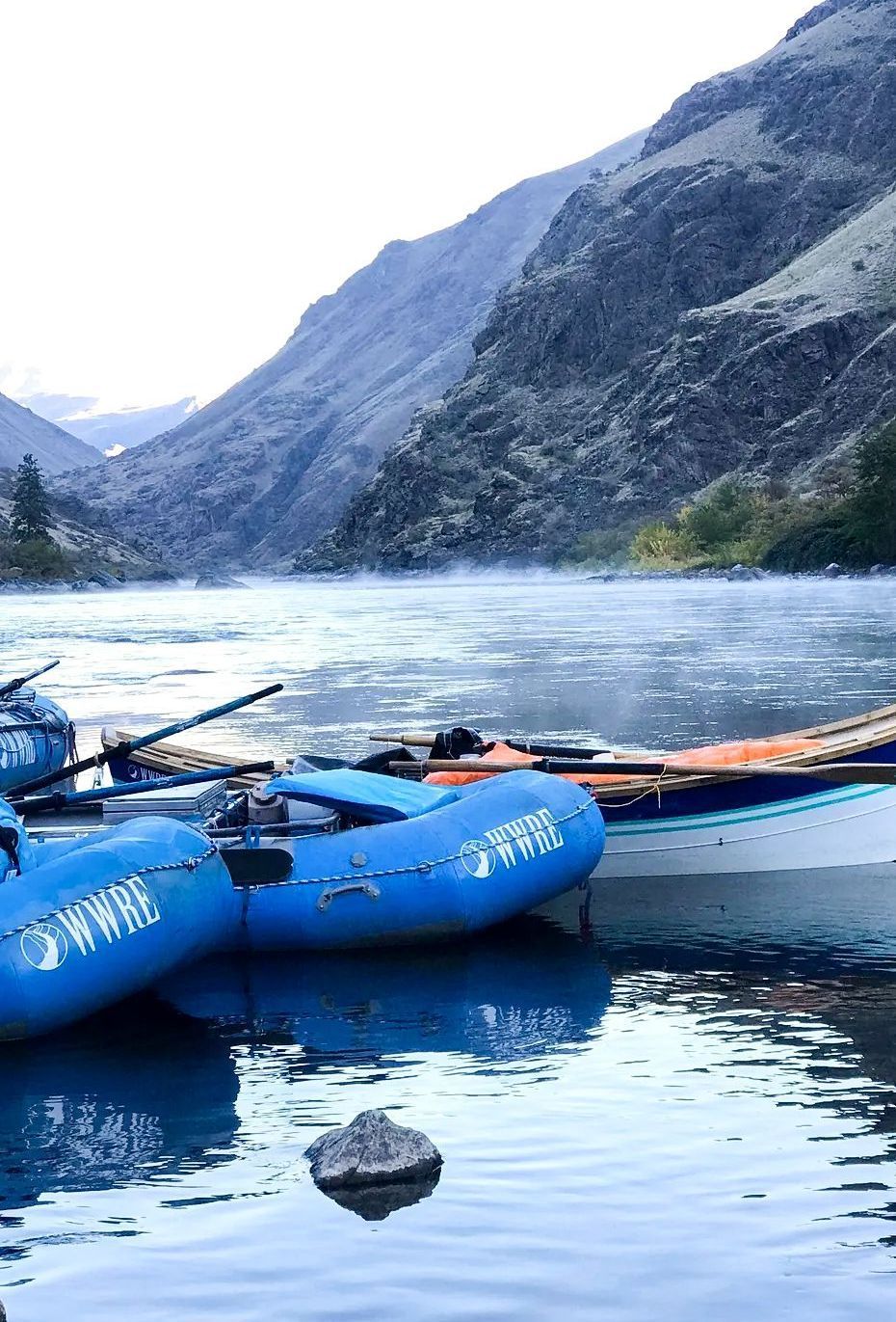 A couple of boats are docked in a river with mountains in the background.