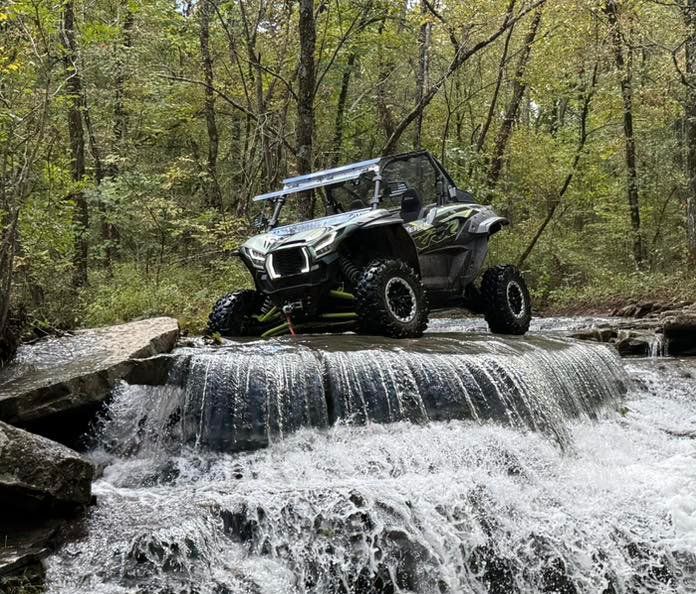 Off-road side-by-side driving over a small waterfall in a forest creek