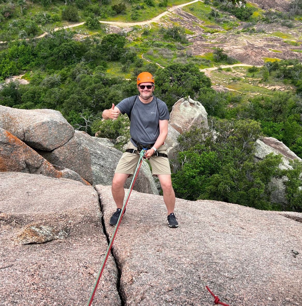 A man is standing on top of a rock holding a rope