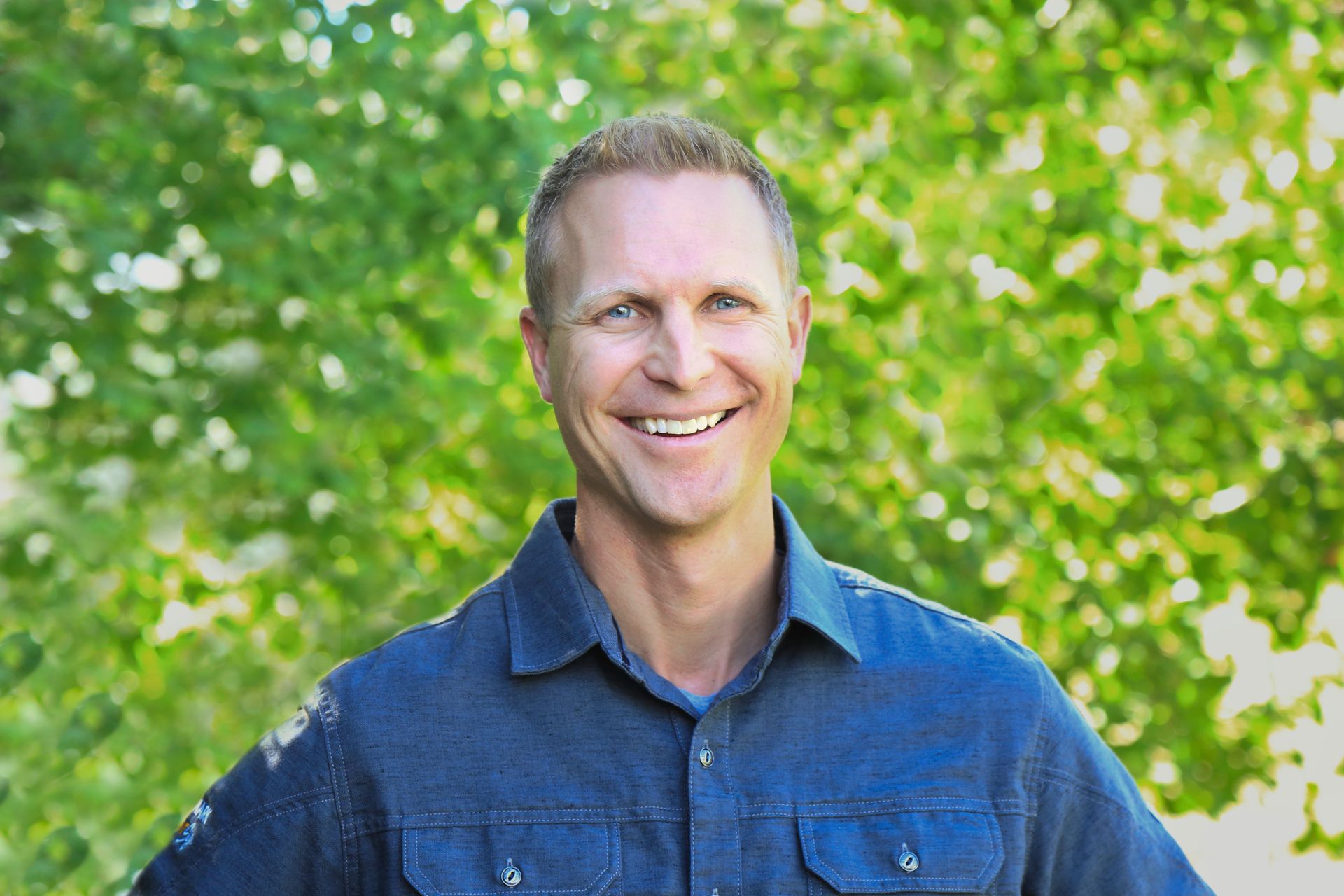 A man wearing a hat and glasses is smiling in front of a canyon.