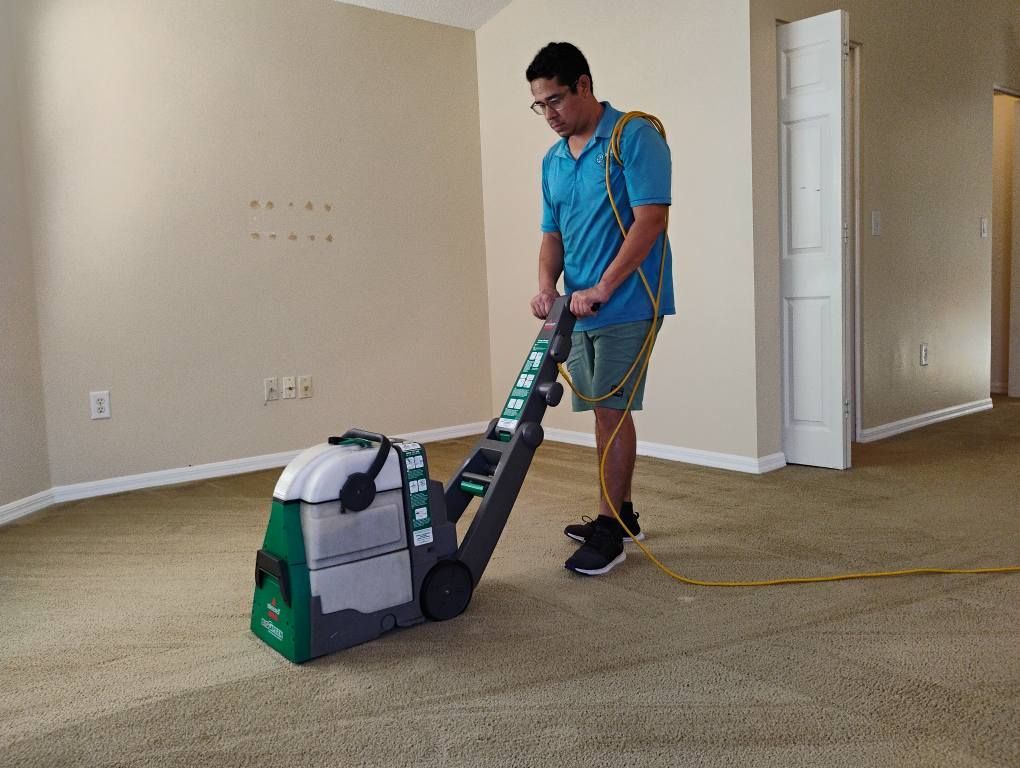 A man is using a vacuum cleaner to clean a carpet in an empty room.
