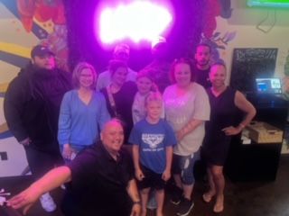 Group of people posing inside a room with a mural. The people include men, women, and a child. A bright light shines behind them.