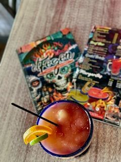 Cocktail with garnish in a blue rimmed glass, menu in the background.