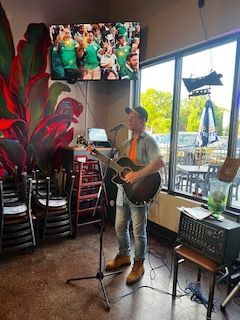 Man singing and playing guitar in bar, watching sports on TV.