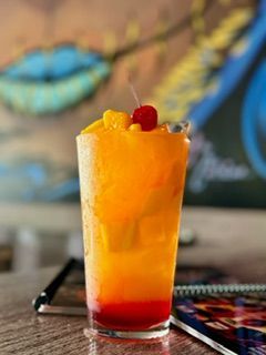 Tall cocktail with layered orange and red liquid, topped with fruit and cherry.