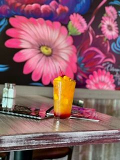 Cocktail in a clear glass with a cherry, on a wooden table against a floral mural.