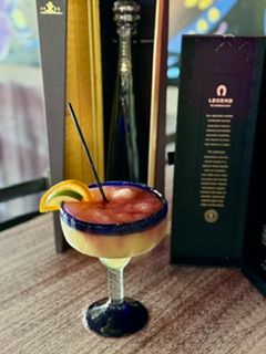 Margarita cocktail with tequila bottle and a box on a wooden table.