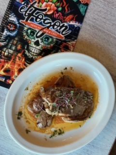 Dish with meat, potatoes, and sauce, next to a restaurant menu.