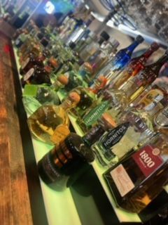 Bar with various tequila bottles lined up, featuring different colors and brands.