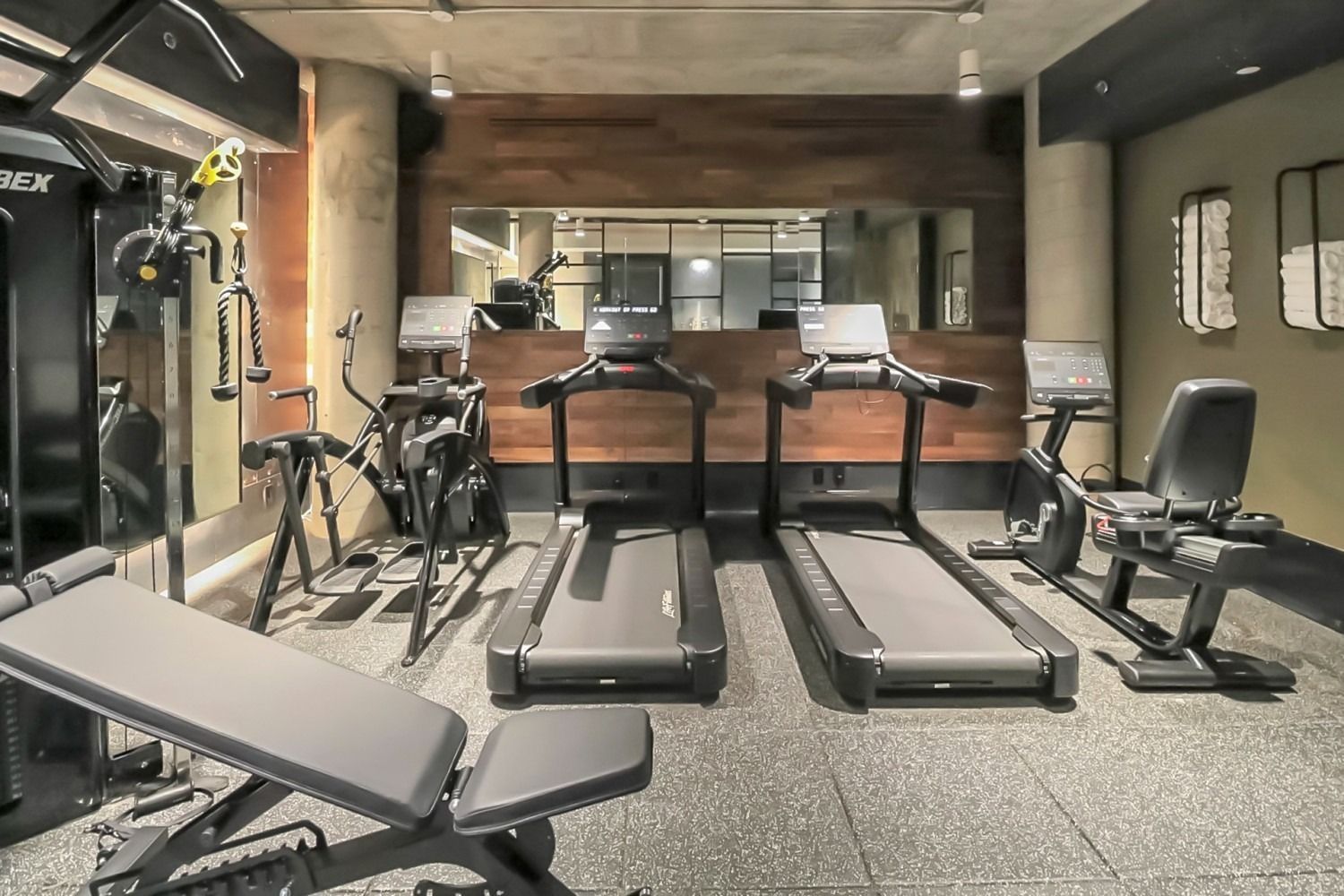 Gym with treadmills, exercise bike, weight bench, and machine. Black and gray equipment on rubber flooring.