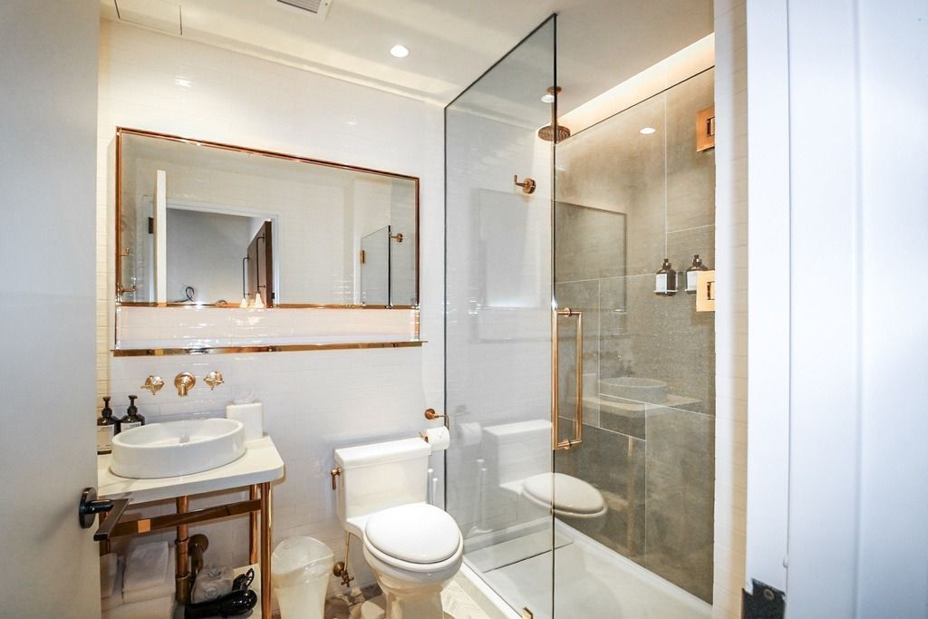 Modern white bathroom with copper accents, glass shower, white sink, and toilet.