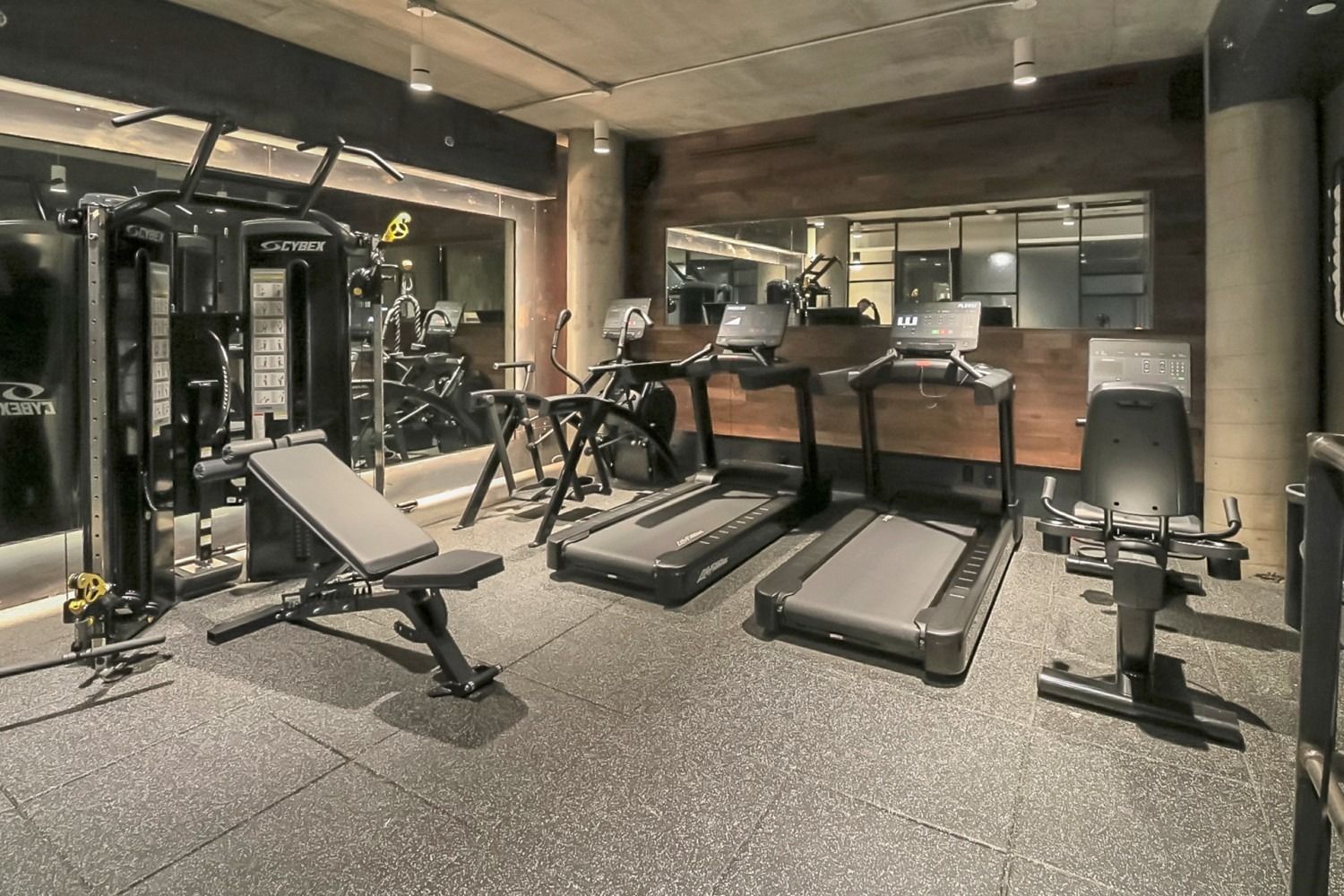 Gym with treadmills, weight machine, bench, and various exercise equipment on rubber flooring.