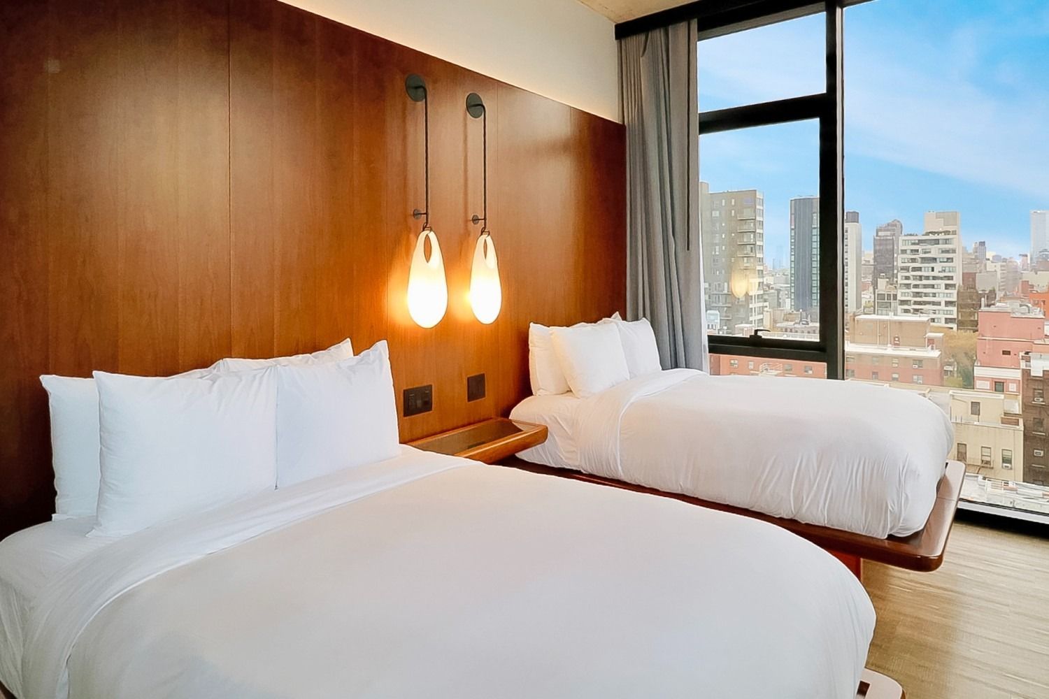 Two white beds in a modern hotel room, with a city view.