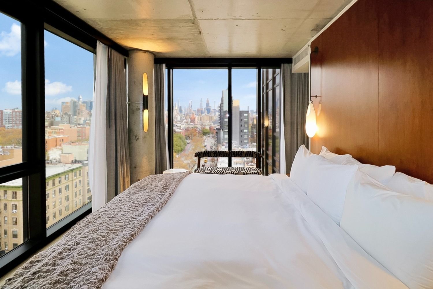 Bedroom with large windows, bed, city view, concrete ceiling, and gray curtains.