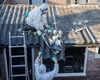 Two men in protective suits are working on the roof of a house.