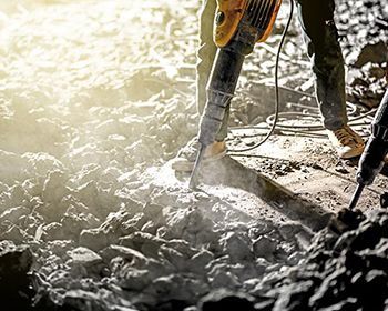 A man is using a hammer to break concrete on a construction site.