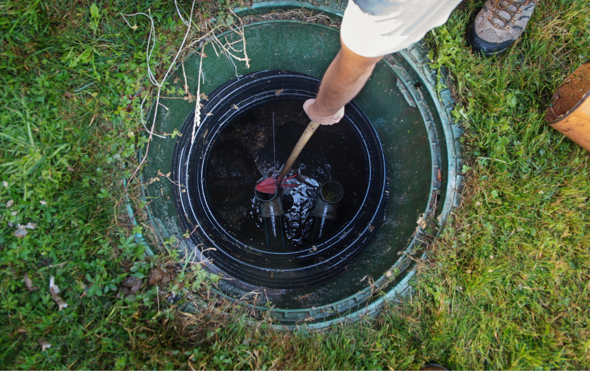 Black septic tank in a rectangular hole in the ground with two green access covers.