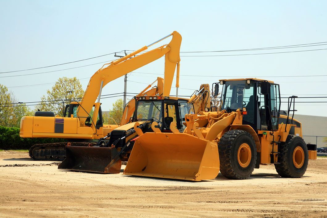 Two yellow construction vehicles are parked next to each other in a dirt field.