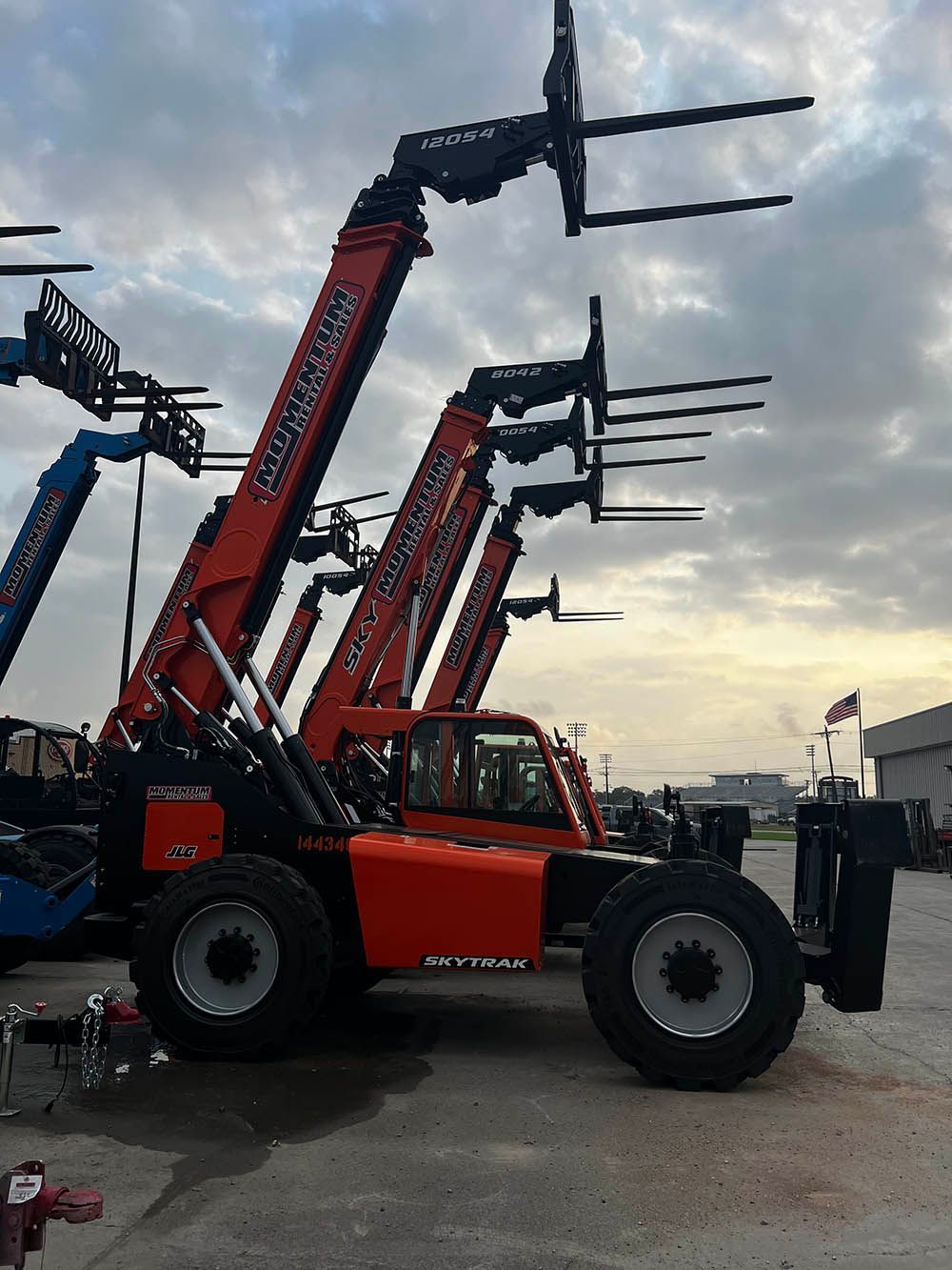 A row of forklifts are parked in a parking lot