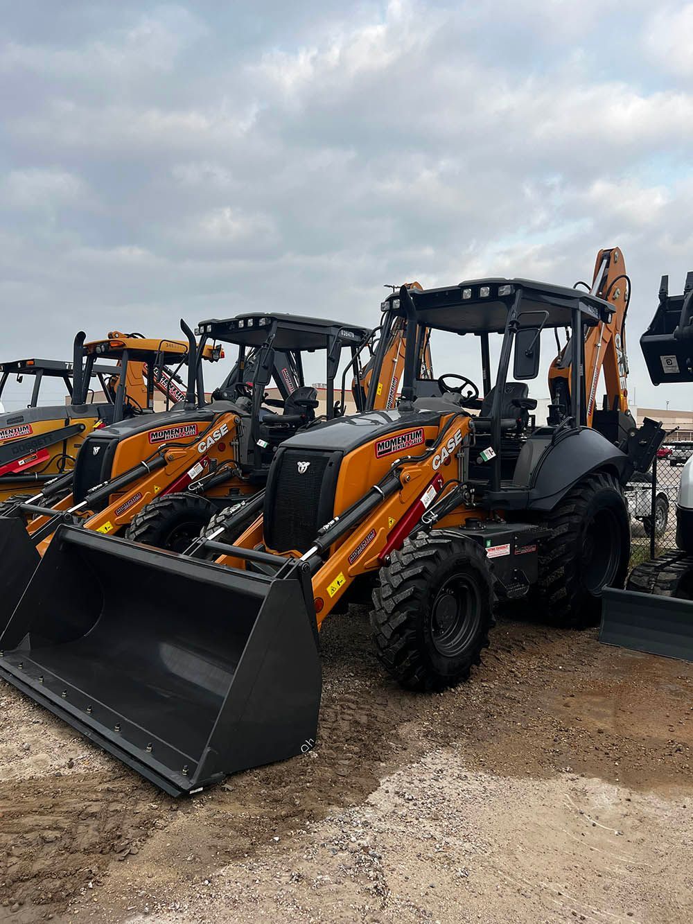 A row of tractors are parked in a dirt field.