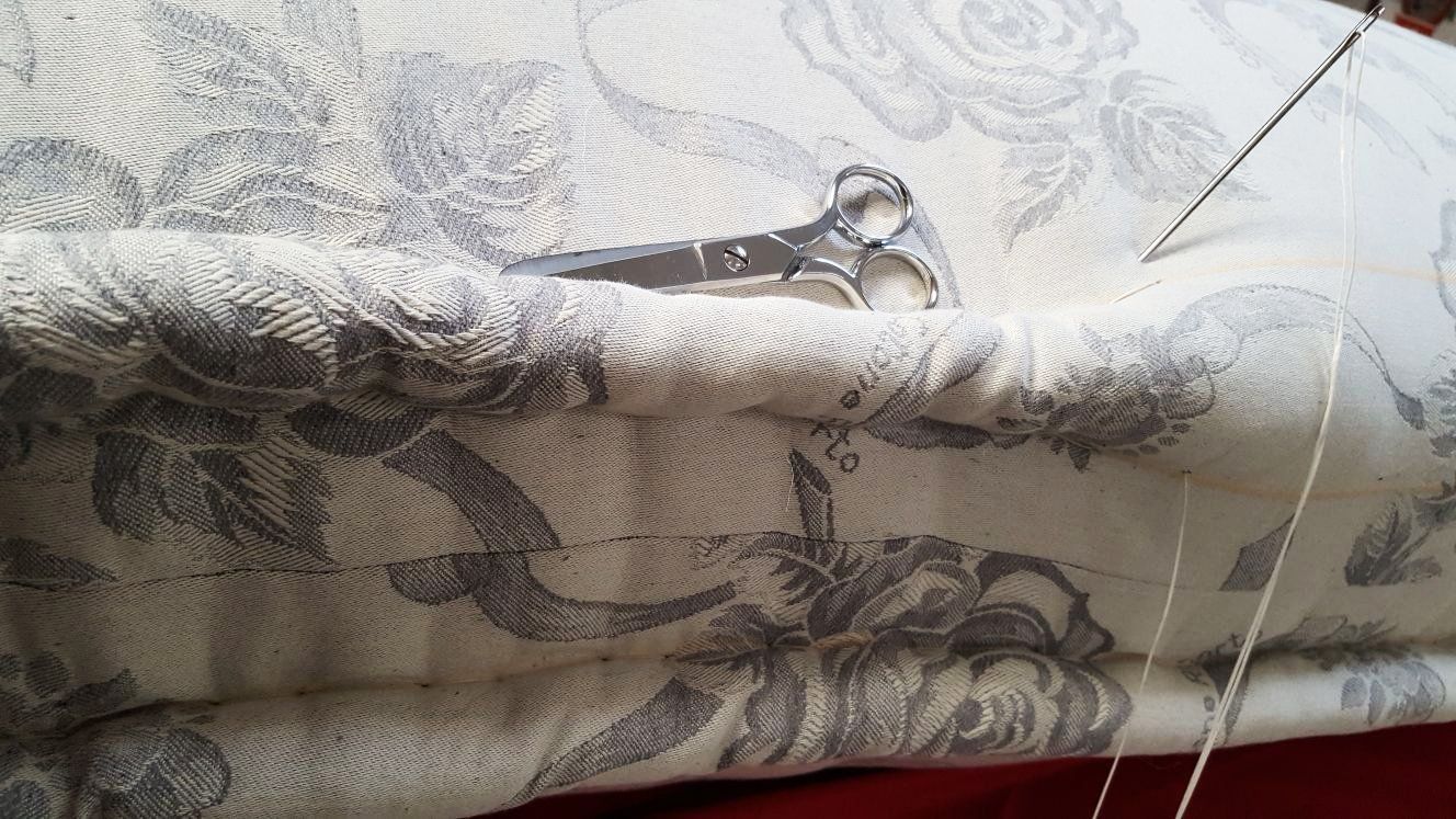 Primo piano del cuscino cucito a mano con ago e filo, con le forbici appoggiate sulla parte superiore. Tessuto floreale grigio.