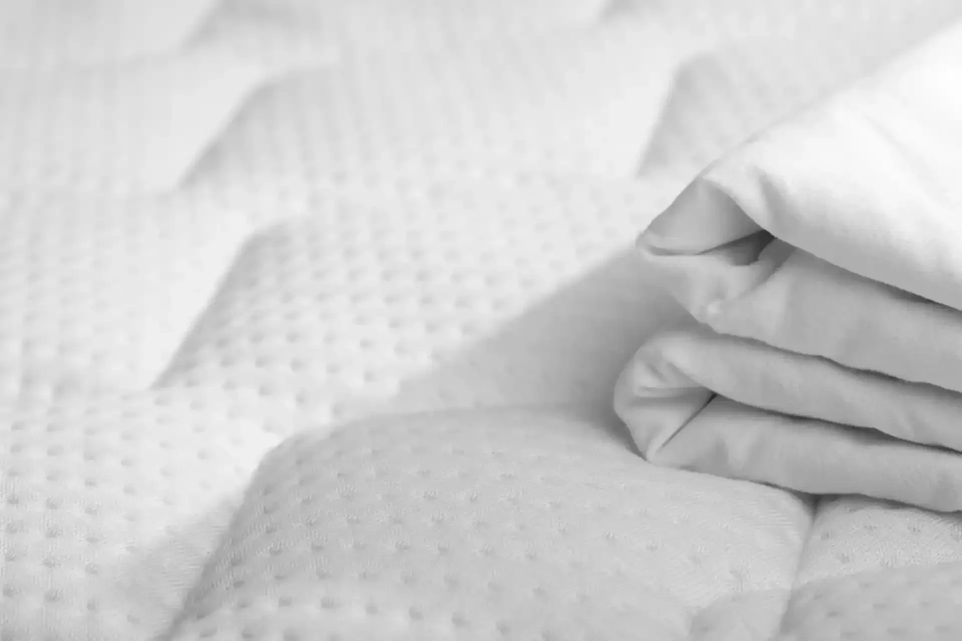 Materasso bianco con lenzuola bianche piegate.