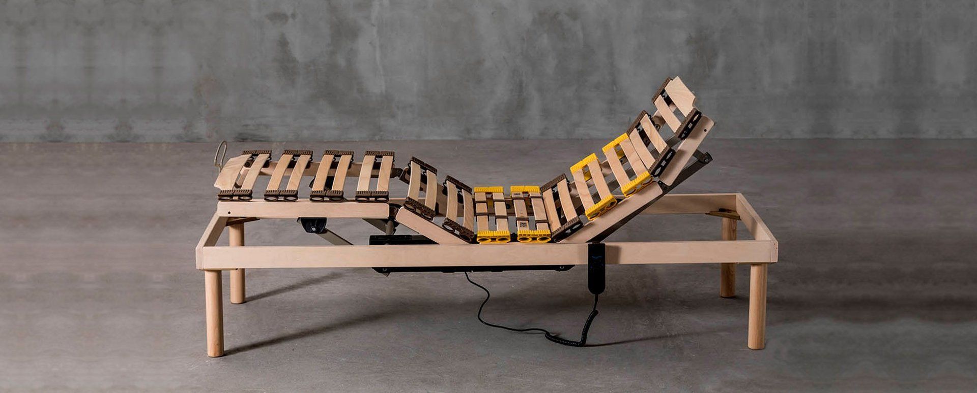 Struttura del letto regolabile in legno, parzialmente rialzata, su sfondo di cemento.