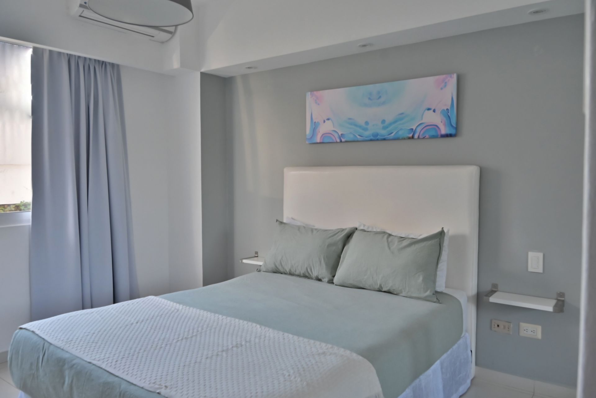 Dormitorio moderno con cama, paredes grises, cortinas azules y arte abstracto en la pared.