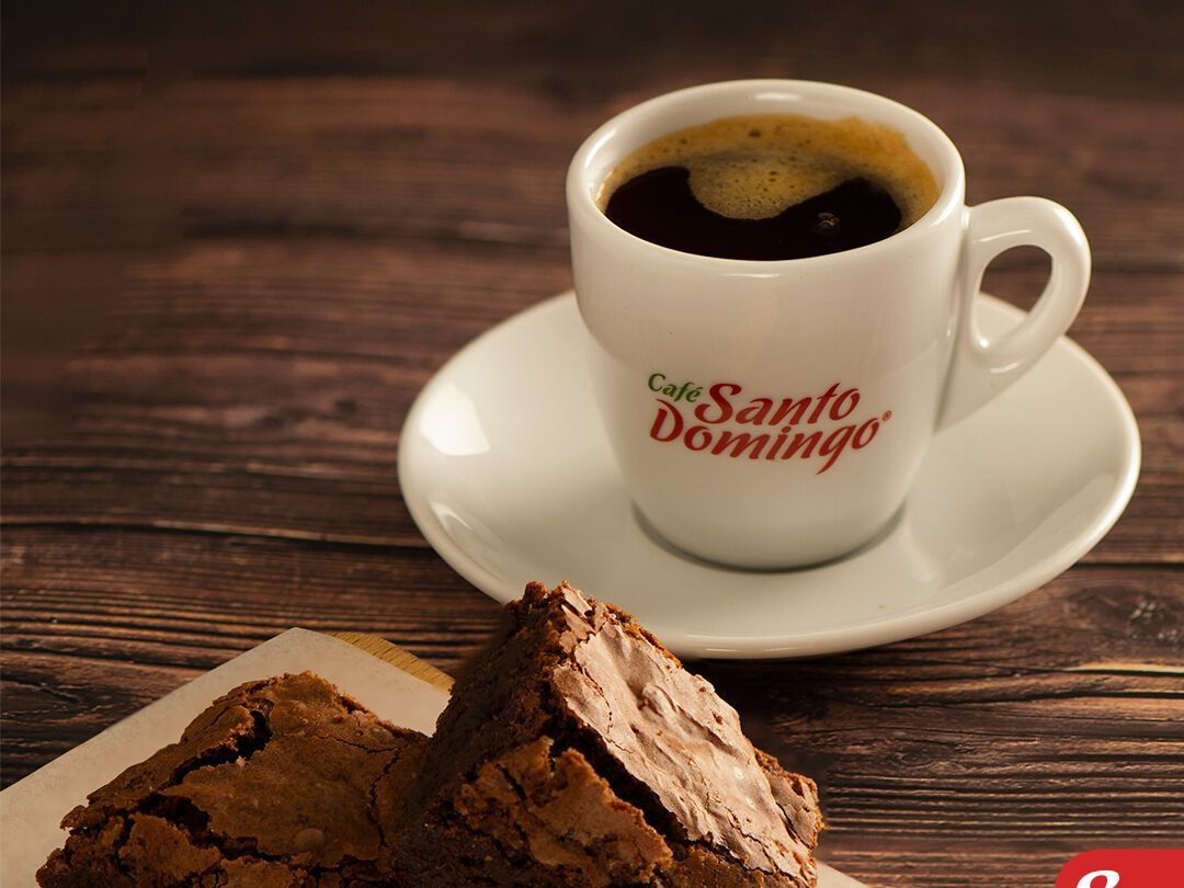 Cafetería luminosa y moderna con mesas, sillas y un mostrador de servicio detrás de estantes de cristal.