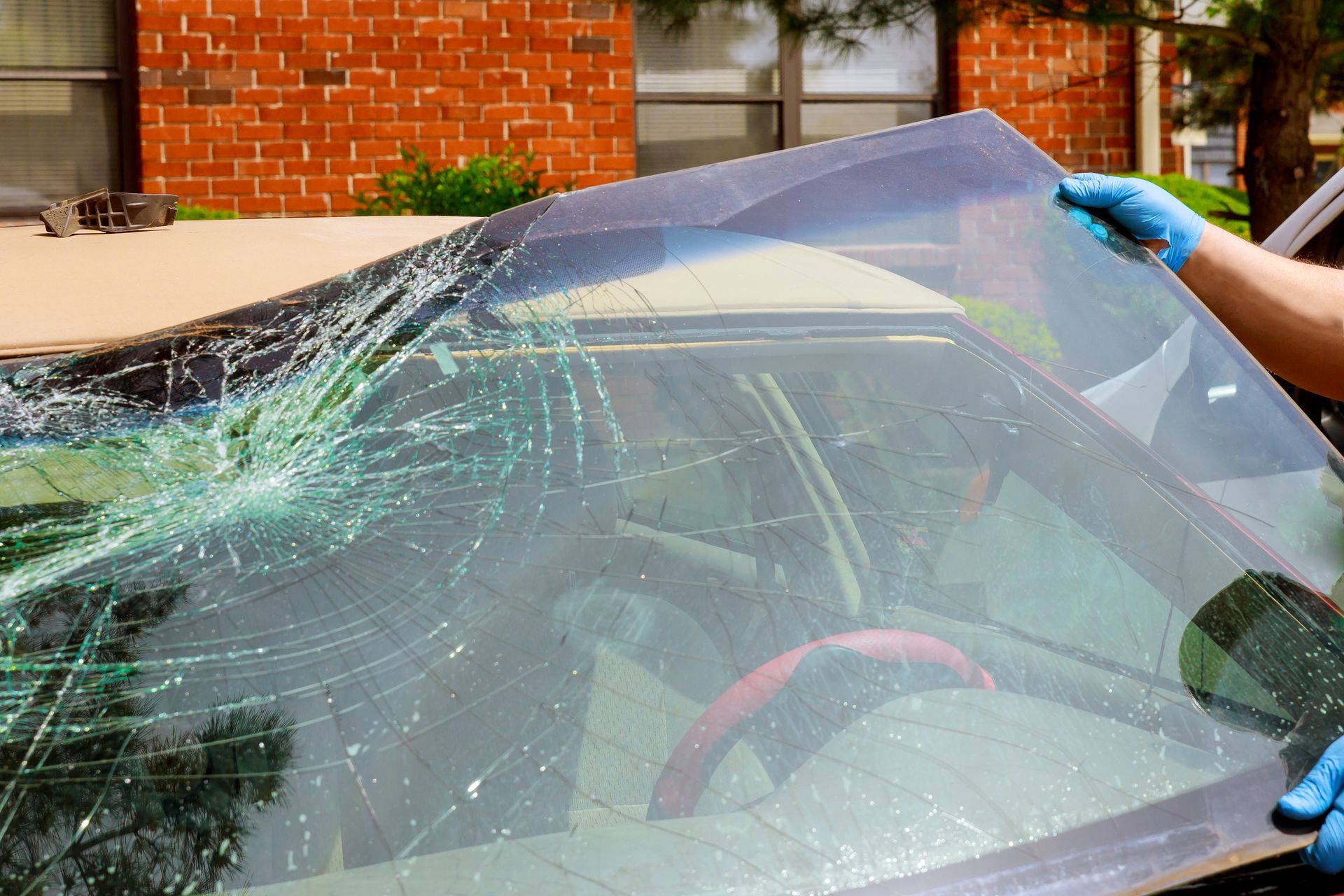Replacing a shattered car windshield. A person in gloves holds the replacement glass over the damaged car.