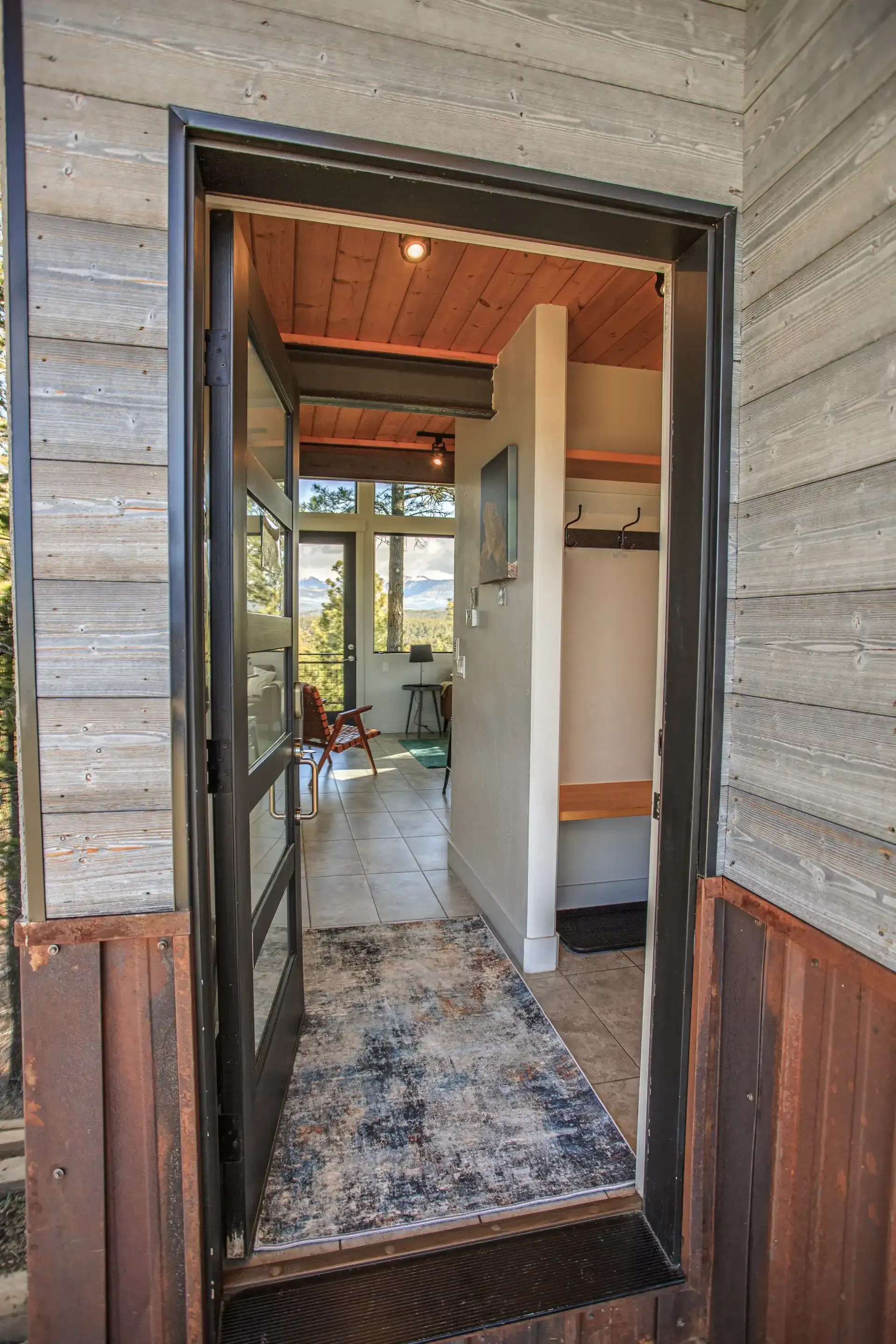 A perspective view through an open doorway looking into a rustic hallway with a patterned rug and a glimpse of a room.