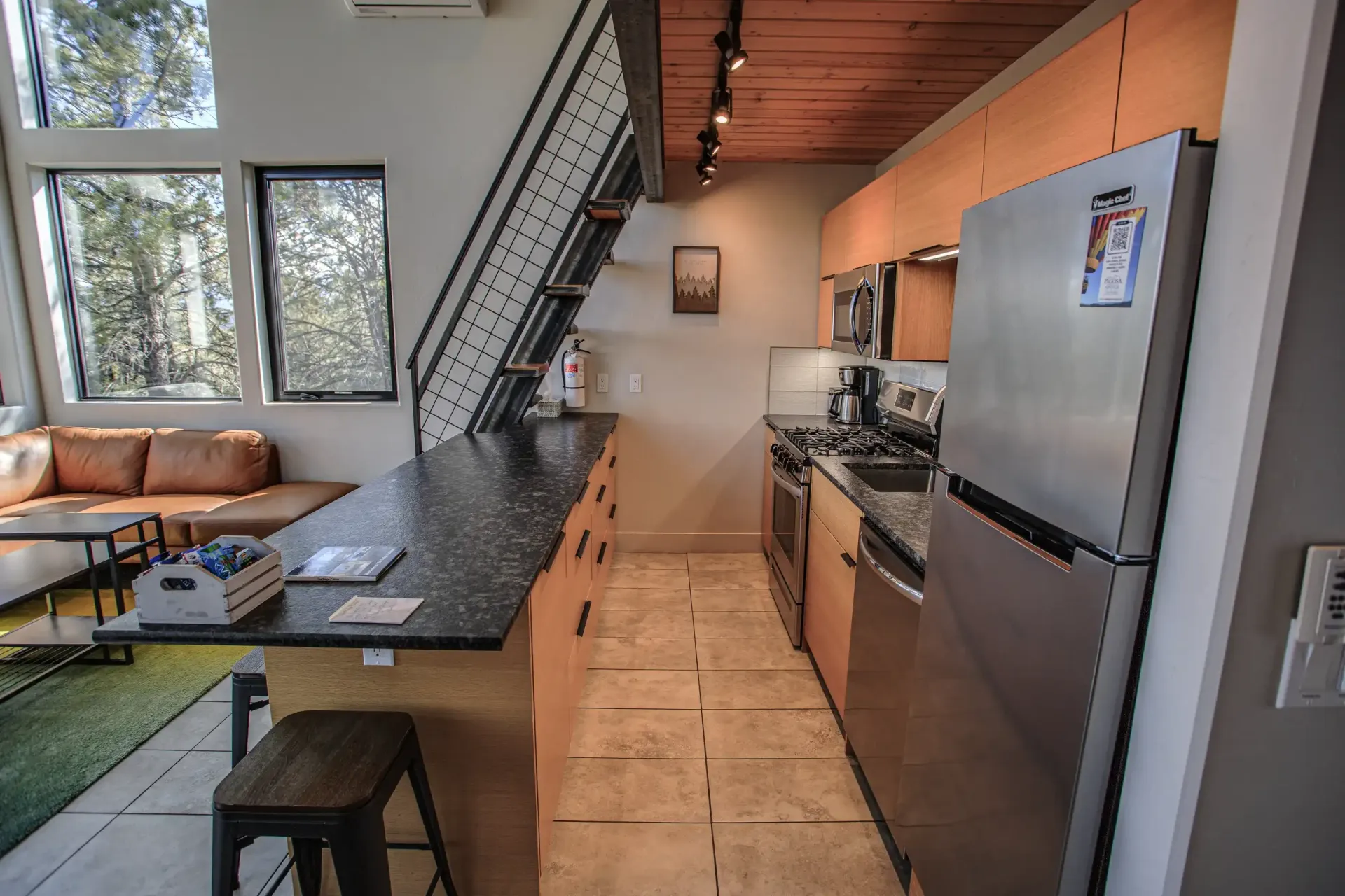 A modern kitchen with a dark granite counter, wood cabinets, stainless steel appliances, and stairs leading to a loft.