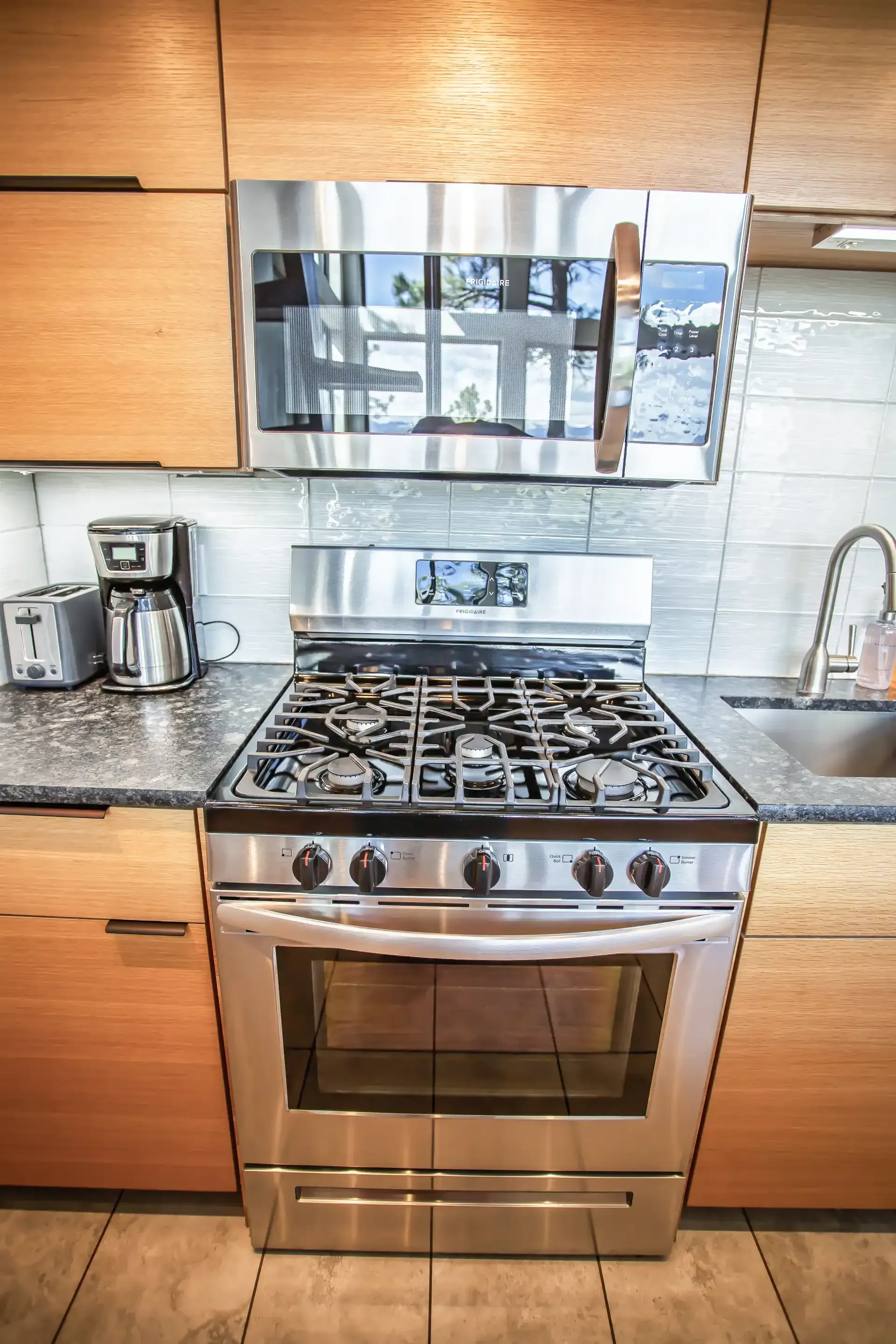 A stainless steel gas stove with a matching microwave above it, situated in a kitchen with light-wood cabinets.
