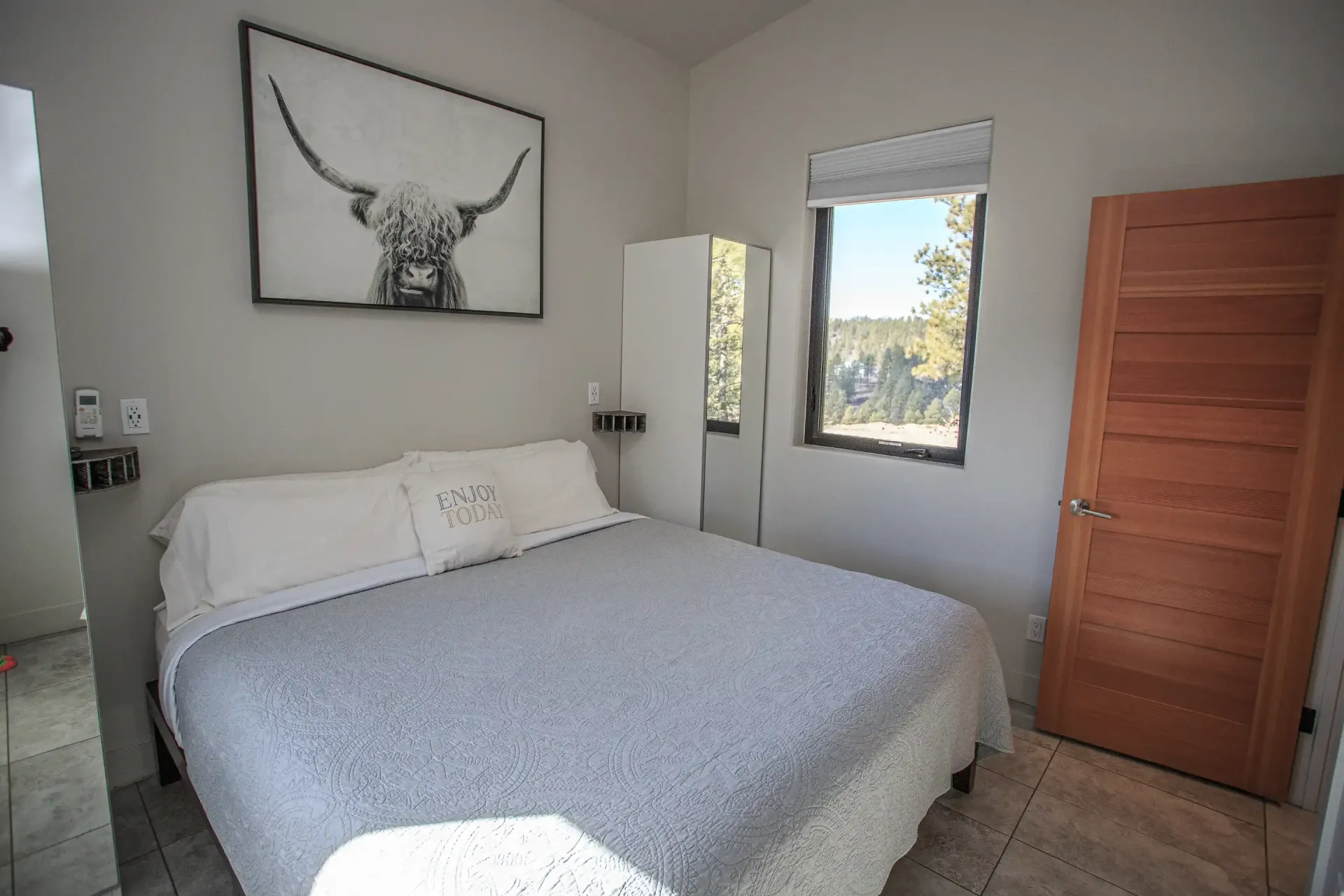 A bedroom with a bed featuring a gray textured quilt, a framed highland cow print on the wall, and a wood door.