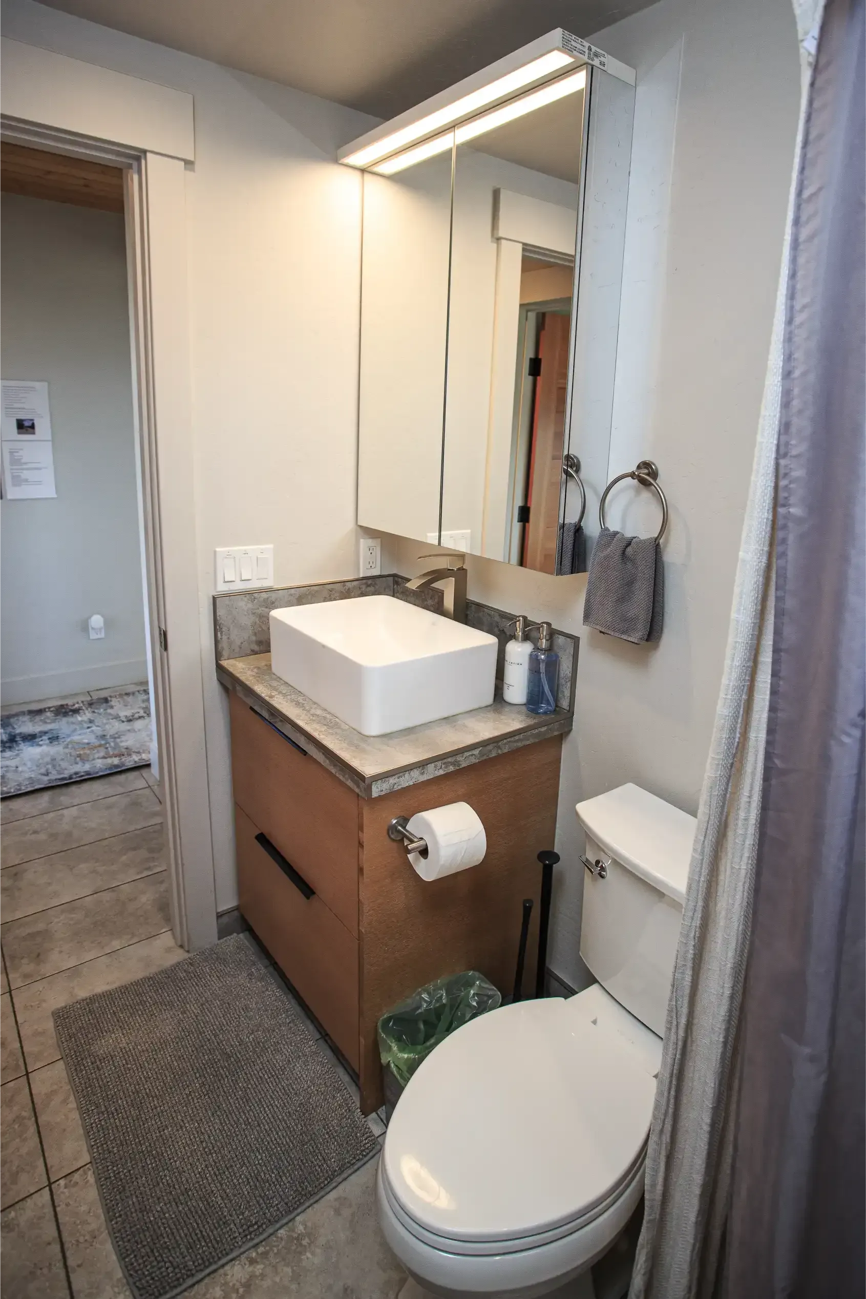 A bathroom featuring a white vessel sink on a wood vanity, a medicine cabinet with lights, and a white toilet.