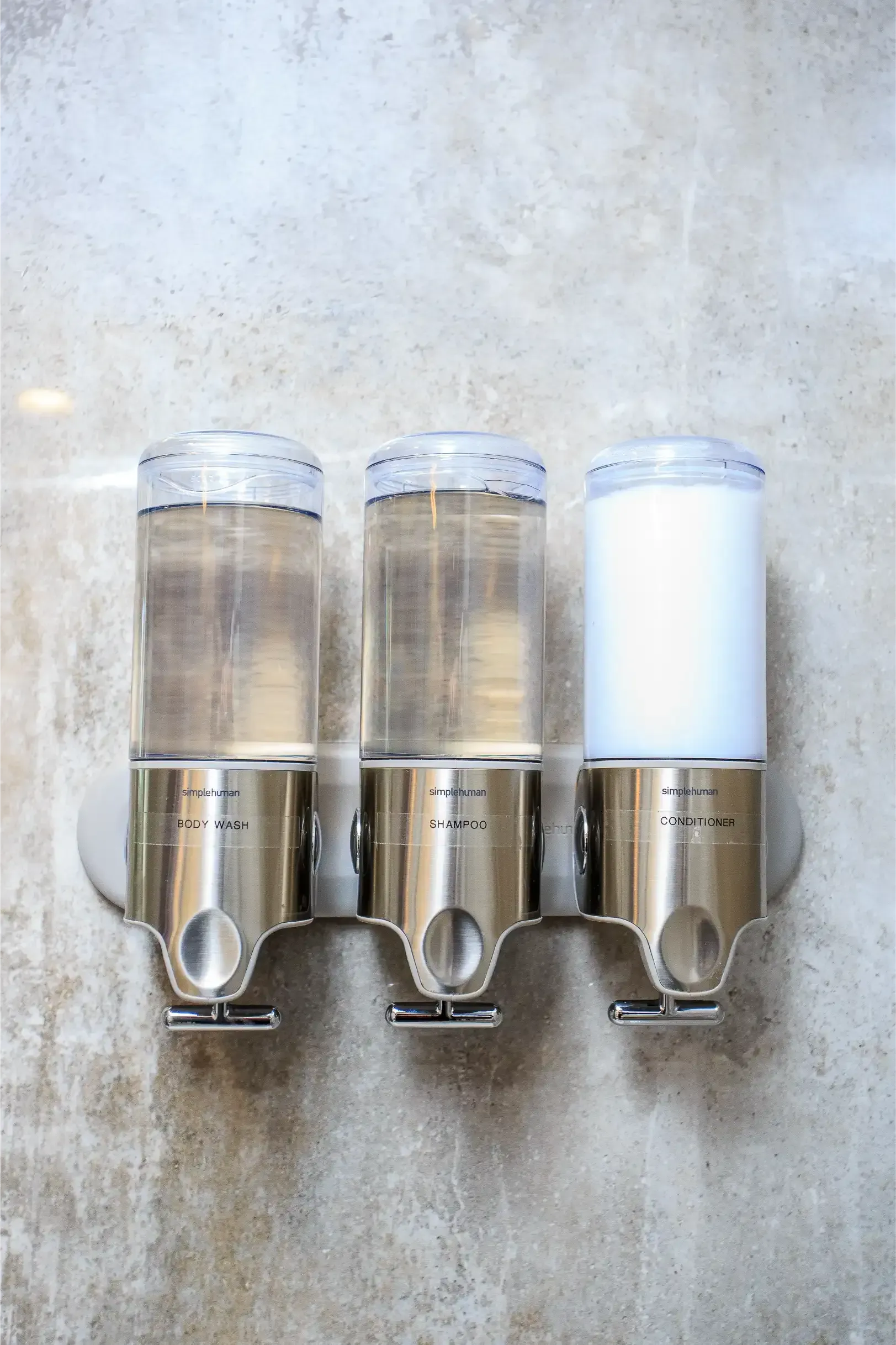 Three clear wall-mounted soap dispensers, with two containing translucent liquid and one filled with white lotion.