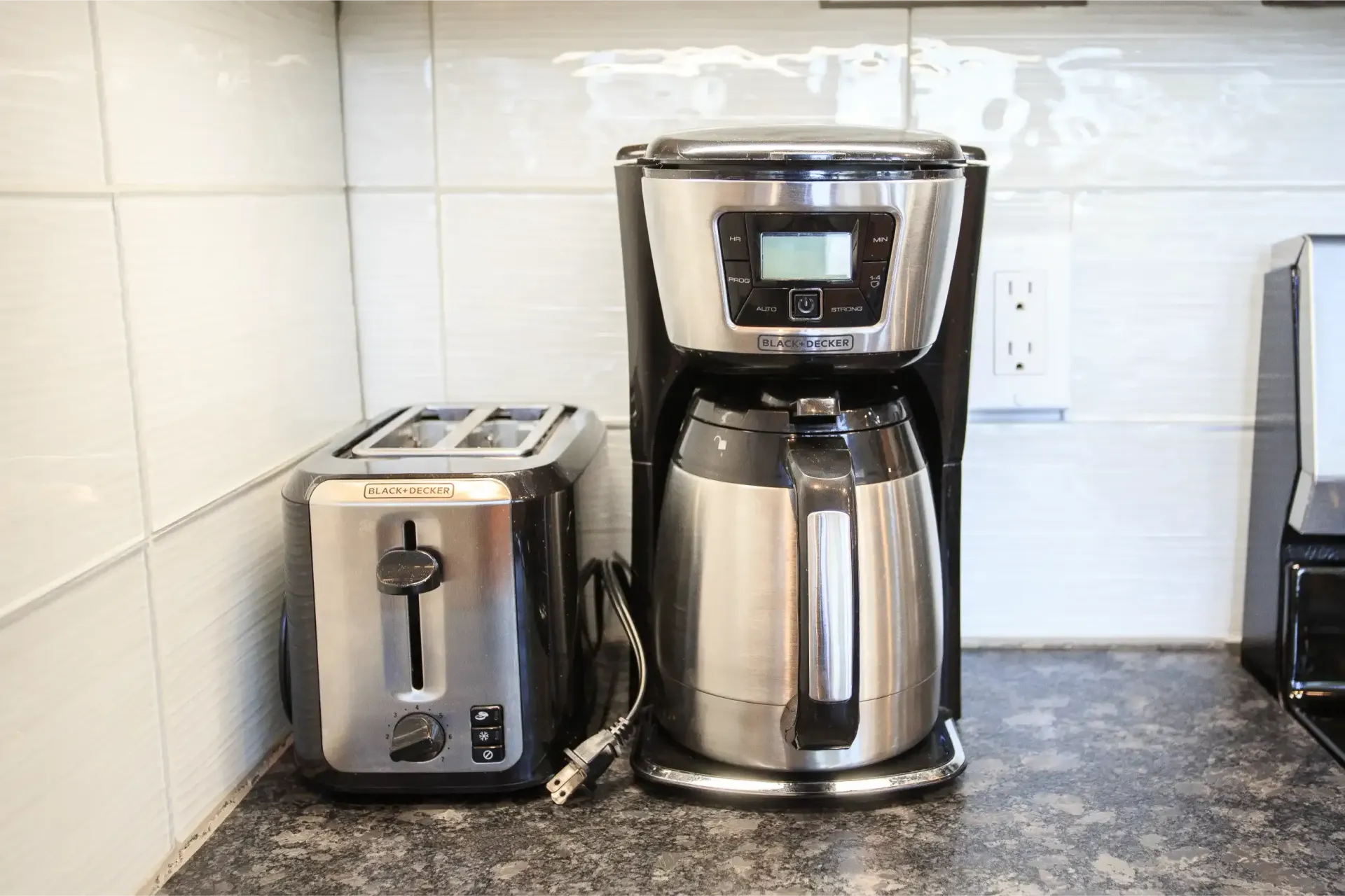 A stainless steel and black coffee maker sits next to a matching two-slice toaster on a dark countertop.