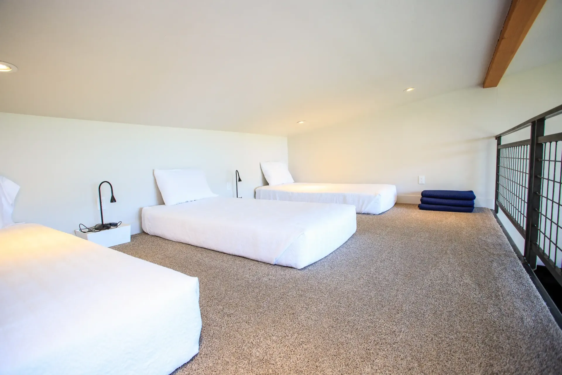 An attic bedroom with a low-sloped ceiling, featuring three single beds with white linens on a light-colored carpet.