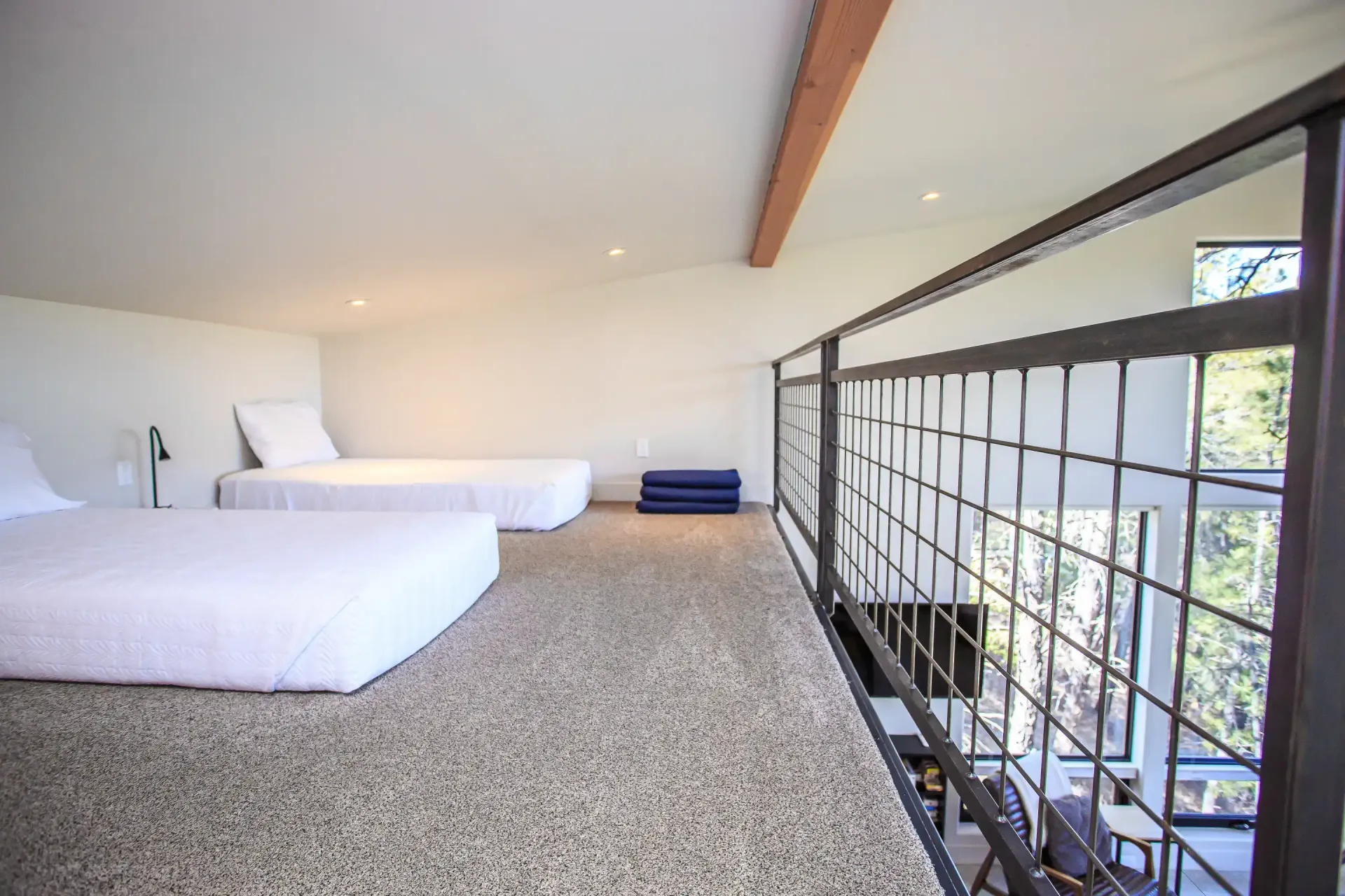 Loft area with two white beds, speckled flooring, and a metal grid railing overlooking a room below.