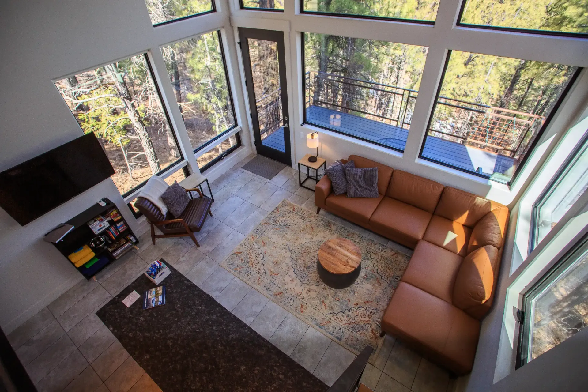 A high-angle view of a modern living room with large windows, a tan leather sectional, an armchair, and a circular table.