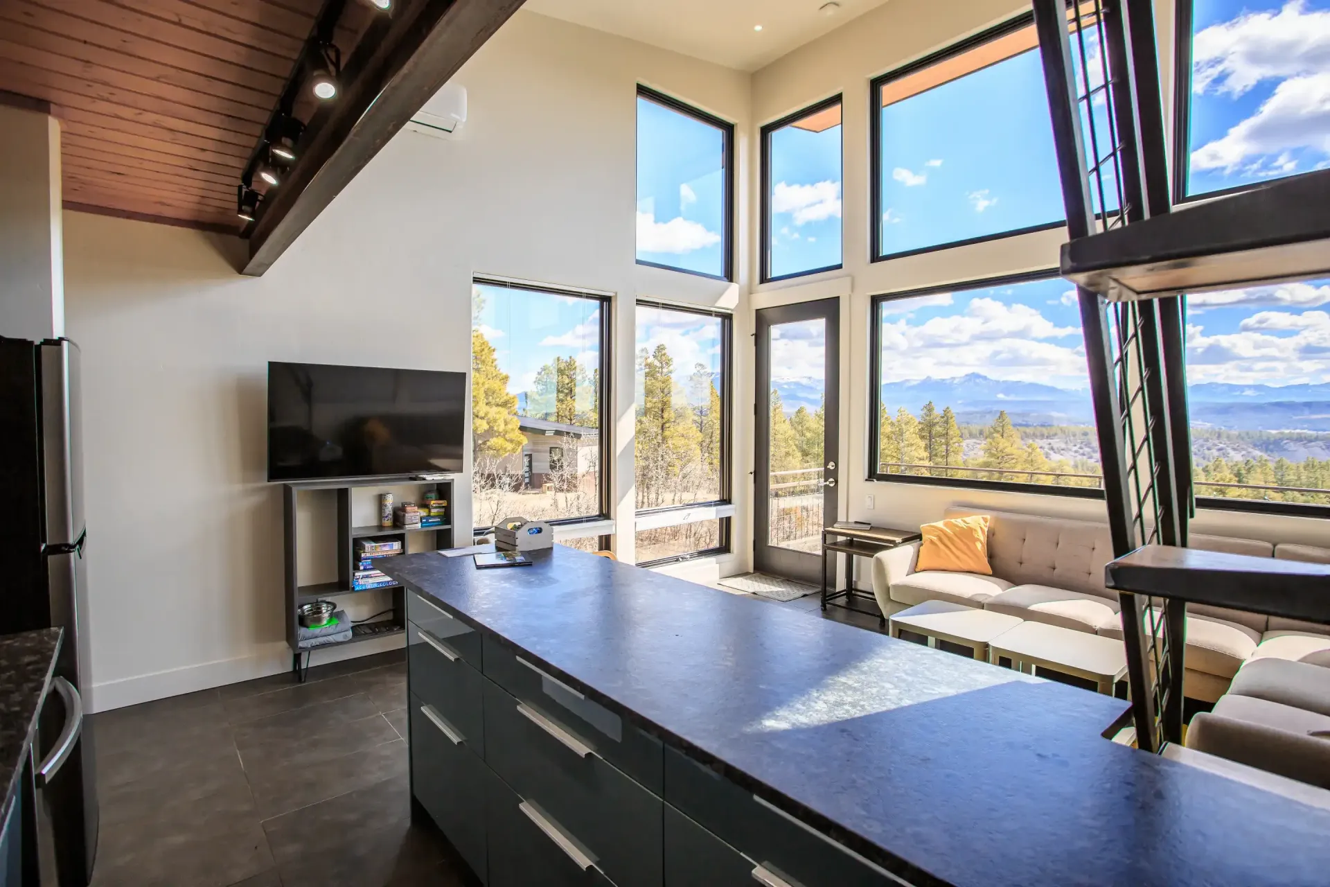Modern kitchen island with dark gray cabinets in a sunlit room featuring floor-to-ceiling windows and a mountain view.