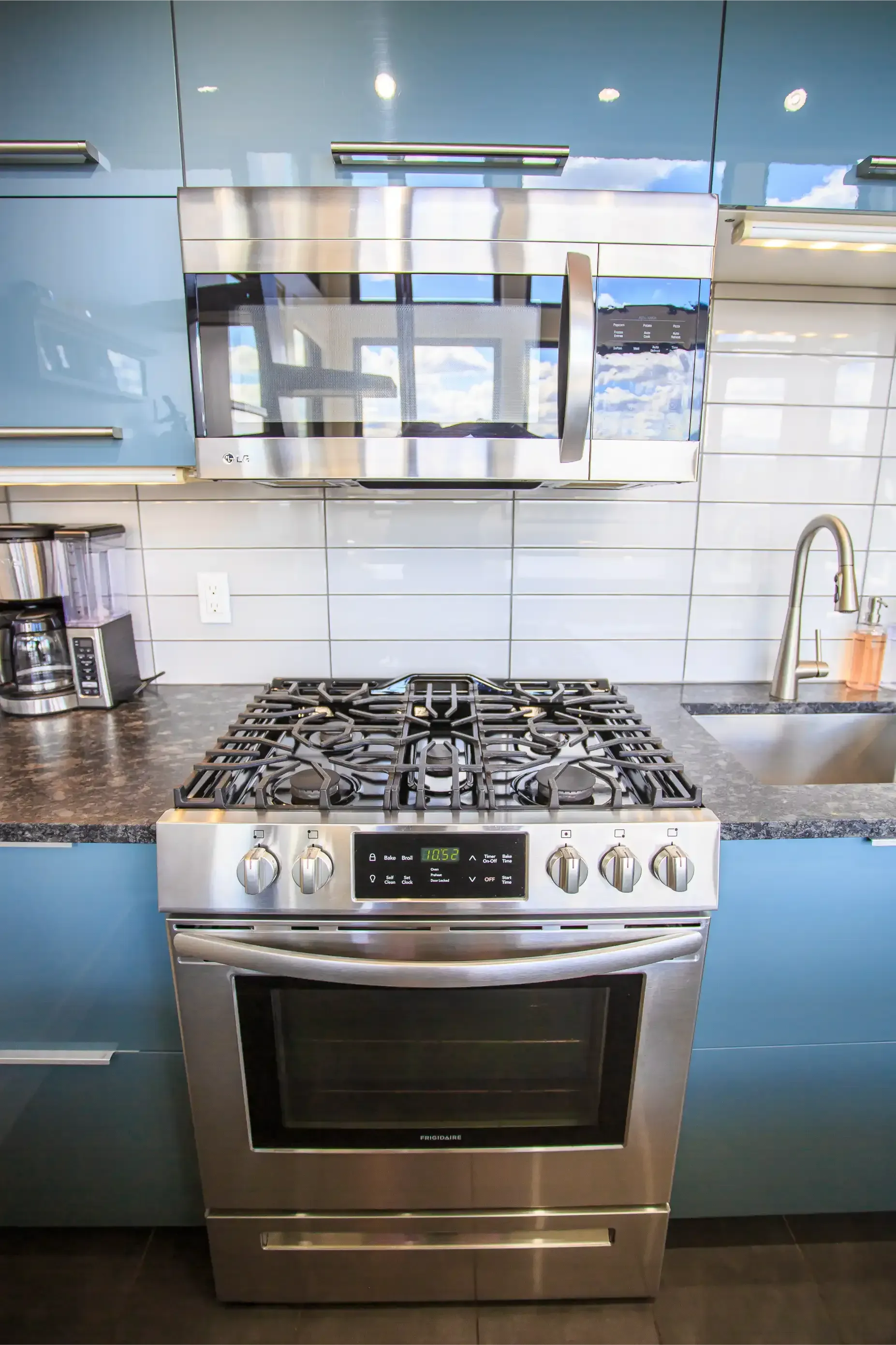 Stainless steel gas range and microwave set against bright blue cabinets and a white subway tile backsplash.