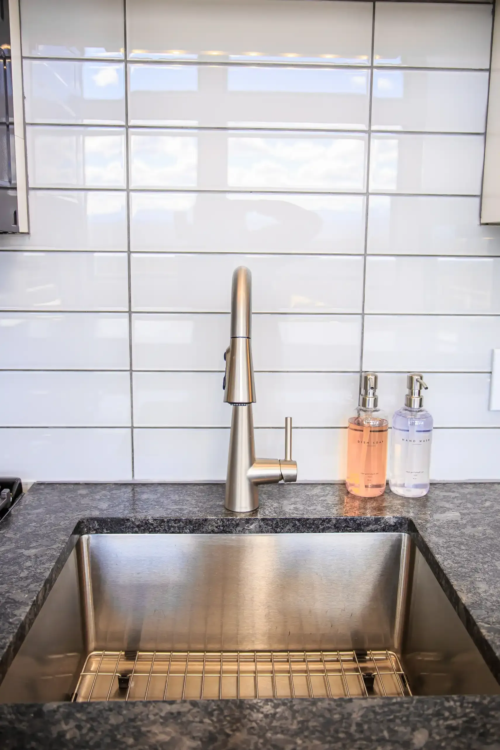 A kitchen sink with a stainless steel faucet and two soap dispensers set against a white subway tile backsplash.